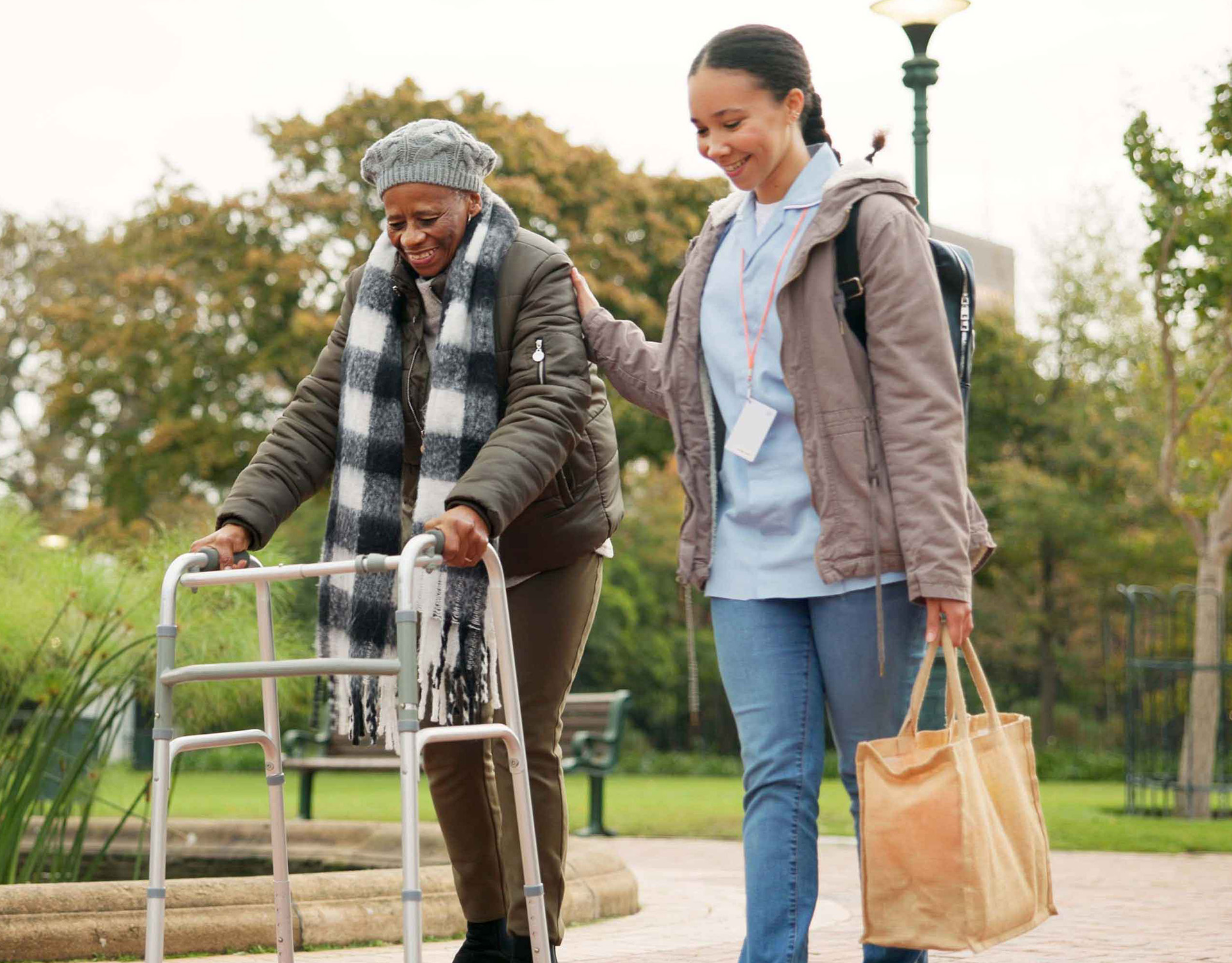 Young woman walking with a woman in a walker outside.
